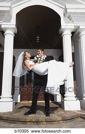 Stock Photography - Young man carrying his bride in his arms in front of a building. Fotosearch