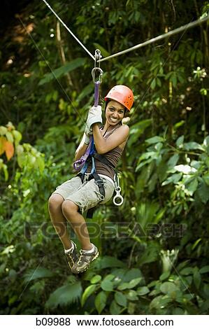 Young woman hanging from a zip-line and smiling View Large Photo Image Stock Photo - Young woman hanging from a zip-line and smiling. Fotosearch