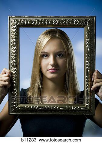 Stock Image - Young woman posing with an empty picture frame. Fotosearch