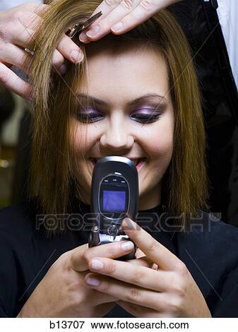 Young woman with cell phone having hair cut smiling View Large Photo Image Stock Photo - Young woman with cell phone having hair cut smiling. Fotosearch