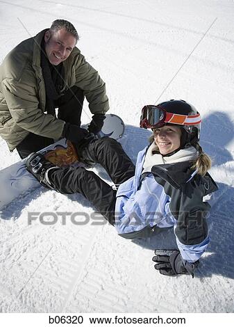 Stock Image - A father helping his daughter with her snowboard. Fotosearch