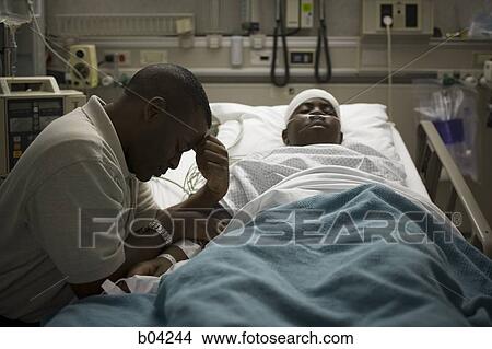 Picture - Boy in hospital bed with head bandages with father by his side. Fotosearch