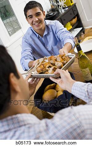 Stock Image - Boy passing chicken to man at table. Fotosearch