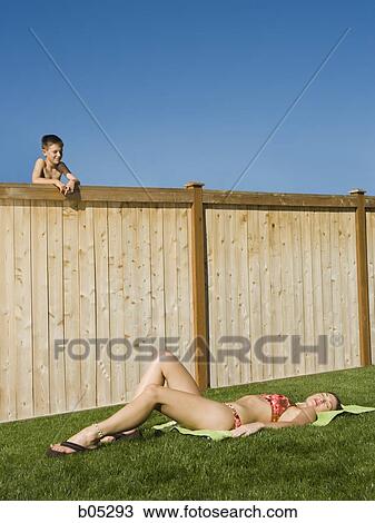 Boy peeping over fence at woman sunbathing View Large Photo Image Stock Image - Boy peeping over fence at woman sunbathing. Fotosearch