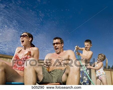 Stock Image - Boy spraying man and woman with hose. Fotosearch
