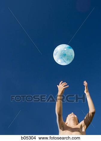 Picture - Boy tossing beach ball with blue sky. Fotosearch