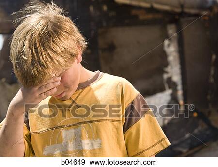 Stock Photo - Boy with burnt house in background. Fotosearch