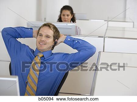 Picture - Businessman in cubicle with headset arms up. Fotosearch
