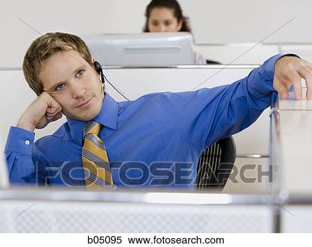 Stock Photography - Businessman in cubicle with headset. Fotosearch