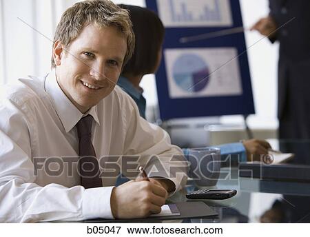 Stock Photo - Businessman making notes at meeting smiling. Fotosearch