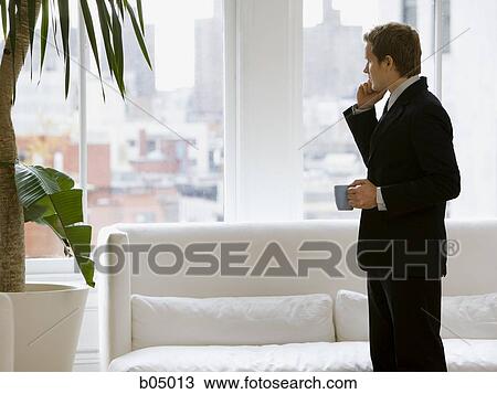 Businessman on cell phone with coffee mug looking out window View Large Photo Image Stock Image - Businessman on cell phone with coffee mug looking out window. Fotosearch