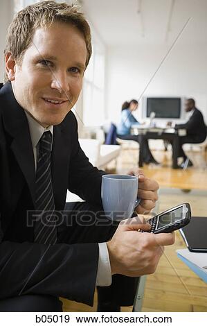 Stock Photo - Businessman with blackberry and coffee mug sitting. Fotosearch