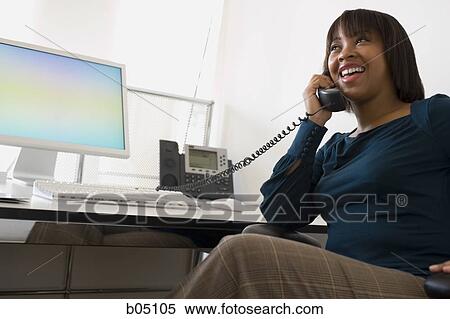Stock Photography - Businesswoman talking on telephone at desk smiling. Fotosearch