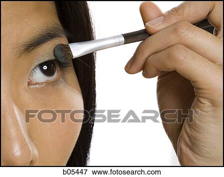 Stock Photo - Closeup of woman applying eyeshadow with makeup brush. Fotosearch