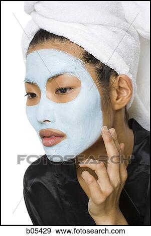 Stock Photo - Closeup of woman applying facial mask with hair towel. Fotosearch