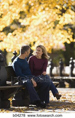 Couple sitting on wooden bench outdoors View Large Photo Image Stock Photo - Couple sitting on wooden bench outdoors. Fotosearch