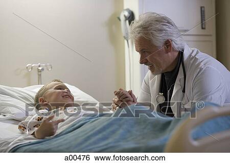 Stock Photograph - Doctor sitting by young boy in hospital bed. Fotosearch