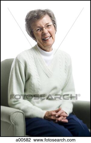 Stock Image - Elderly woman sitting in an armchair smiling. Fotosearch