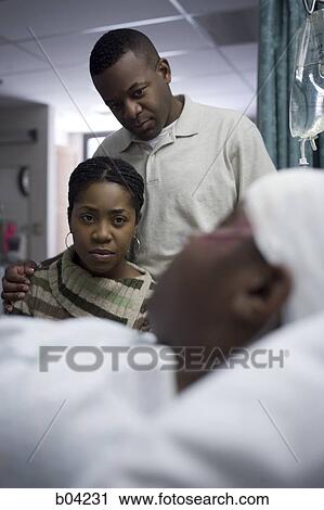 Stock Image - Family watching boy in hospital bed with head bandages. Fotosearch
