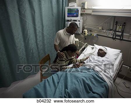 Stock Image - Family watching boy in hospital bed with head bandages. Fotosearch