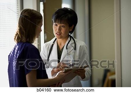 Stock Image - Female doctor explaining patient records to nurse. Fotosearch
