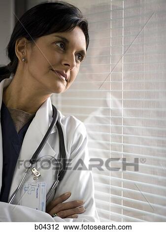 Stock Image - Female doctor leaning on window with blinds. Fotosearch