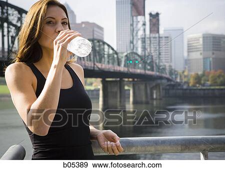 Stock Photo - Female drinking bottled water outdoors with city skyline. Fotosearch