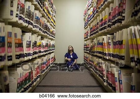 Stock Photograph - Female nurse sitting on floor looking at patient records. Fotosearch
