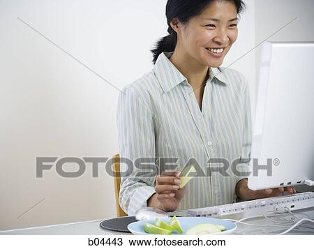 Stock Image - Female sitting at desk with computer. Fotosearch
