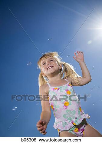 Girl in swimsuit catching bubbles outdoors with blue sky View Large Photo Image Stock Photo - Girl in swimsuit catching bubbles outdoors with blue sky. Fotosearch