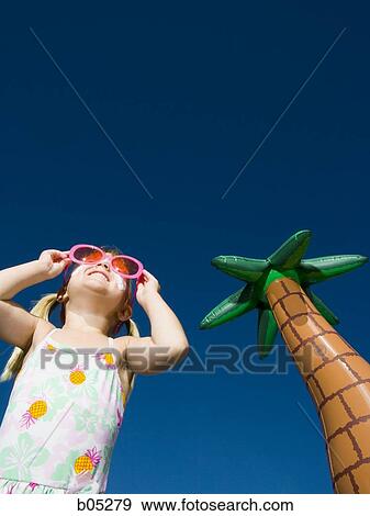 Girl with suntan lotion and sunglasses smiling with inflatable palm tree View Large Photo Image Stock Photo - Girl with suntan lotion and sunglasses smiling with inflatable palm tree. Fotosearch
