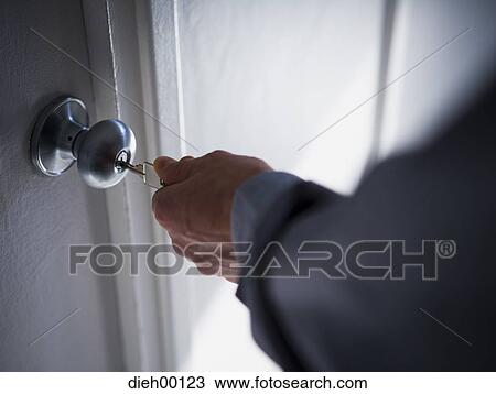 Stock Image - Hand putting a key into a door lock. Fotosearch