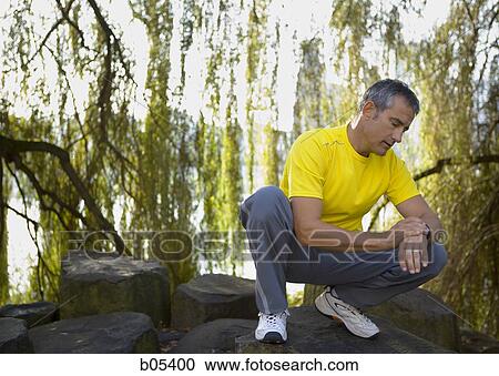 Male jogger squatting and checking watch View Large Photo Image Stock Image - Male jogger squatting and checking watch. Fotosearch