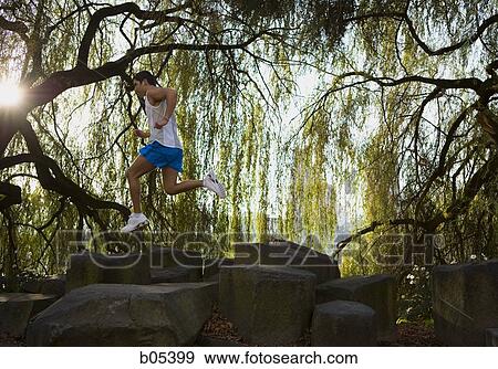 Stock Photo - Male jogging over rocks in forest. Fotosearch
