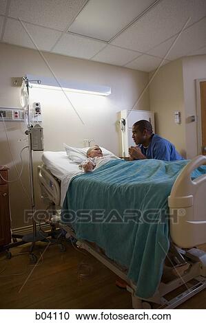 Stock Image - Male nurse sitting by boy in hospital bed. Fotosearch
