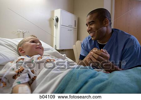 Stock Photo - Male nurse sitting by boy in hospital bed. Fotosearch