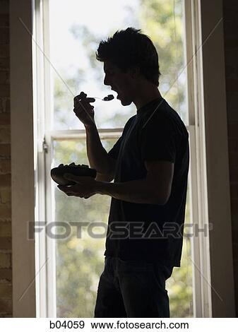 Stock Photo - Man in front of window eating bowl of cereal. Fotosearch