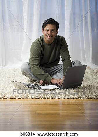 Picture - Man on carpet with laptop smiling. Fotosearch
