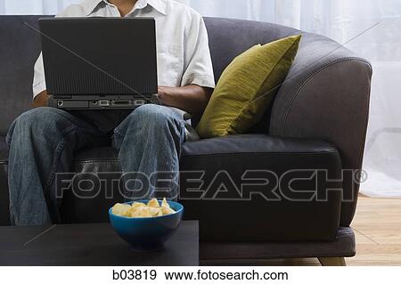 Man on sofa with laptop and bowl of potato chips View Large Photo Image Stock Photo - Man on sofa with laptop and bowl of potato chips. Fotosearch