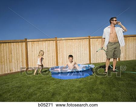 Man with hose talking on cell phone spraying boy with hose in children's pool View Large Photo Image Stock Image - Man with hose talking on cell phone spraying boy with hose in children's pool. Fotosearch