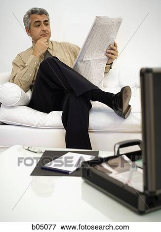 Stock Photo - Mature businessman sitting on sofa reading newspaper. Fotosearch