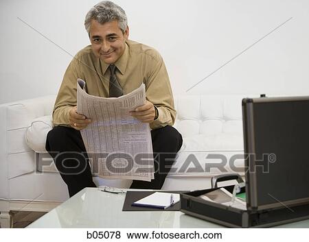 Stock Photo - Mature businessman sitting on sofa with newspaper smiling. Fotosearch