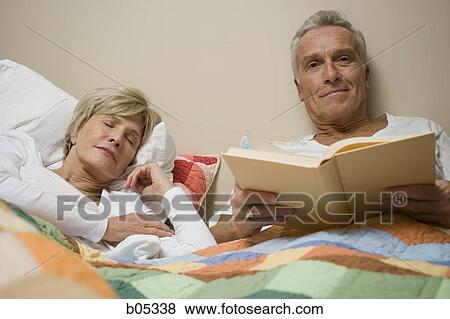 Mature man in bed reading with sleeping woman View Large Photo Image Stock Photo - Mature man in bed reading with sleeping woman. Fotosearch