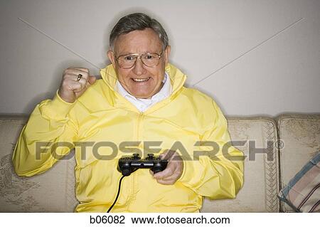 Mature man sitting on a couch playing a videogame View Large Photo Image Stock Image - Mature man sitting on a couch playing a videogame. Fotosearch
