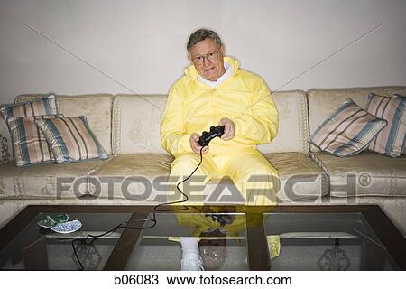 Stock Image - Mature man sitting on a couch playing a videogame. Fotosearch