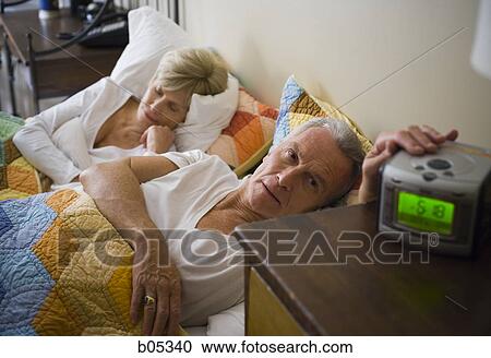 Mature man with alarm clock in bed with sleeping mature woman View Large Photo Image Stock Image - Mature man with alarm clock in bed with sleeping mature woman. Fotosearch
