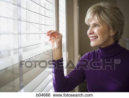 Mature woman looking through window View Large Photo Image Stock Photograph - Mature woman looking through window. Fotosearch