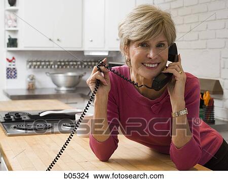 Mature woman talking on telephone in kitchen View Large Photo Image Picture - Mature woman talking on telephone in kitchen. Fotosearch