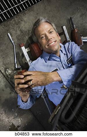 Stock Image - Mechanic under car smiling with wedding ring. Fotosearch