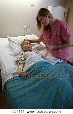 Stock Image - Nurse talking to boy in hospital bed. Fotosearch